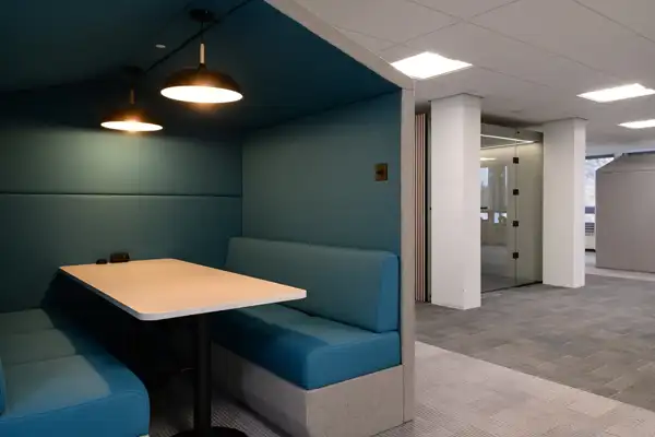 Pitched roof office booth with built-in seating, table and lamps